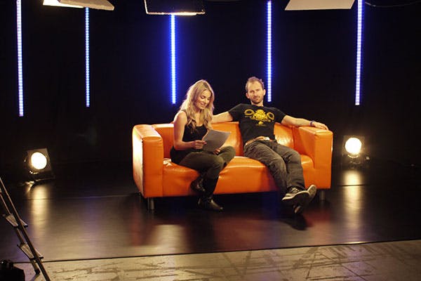 Live TV studio with presenters on orange couch, ideal for interviews and broadcasts.