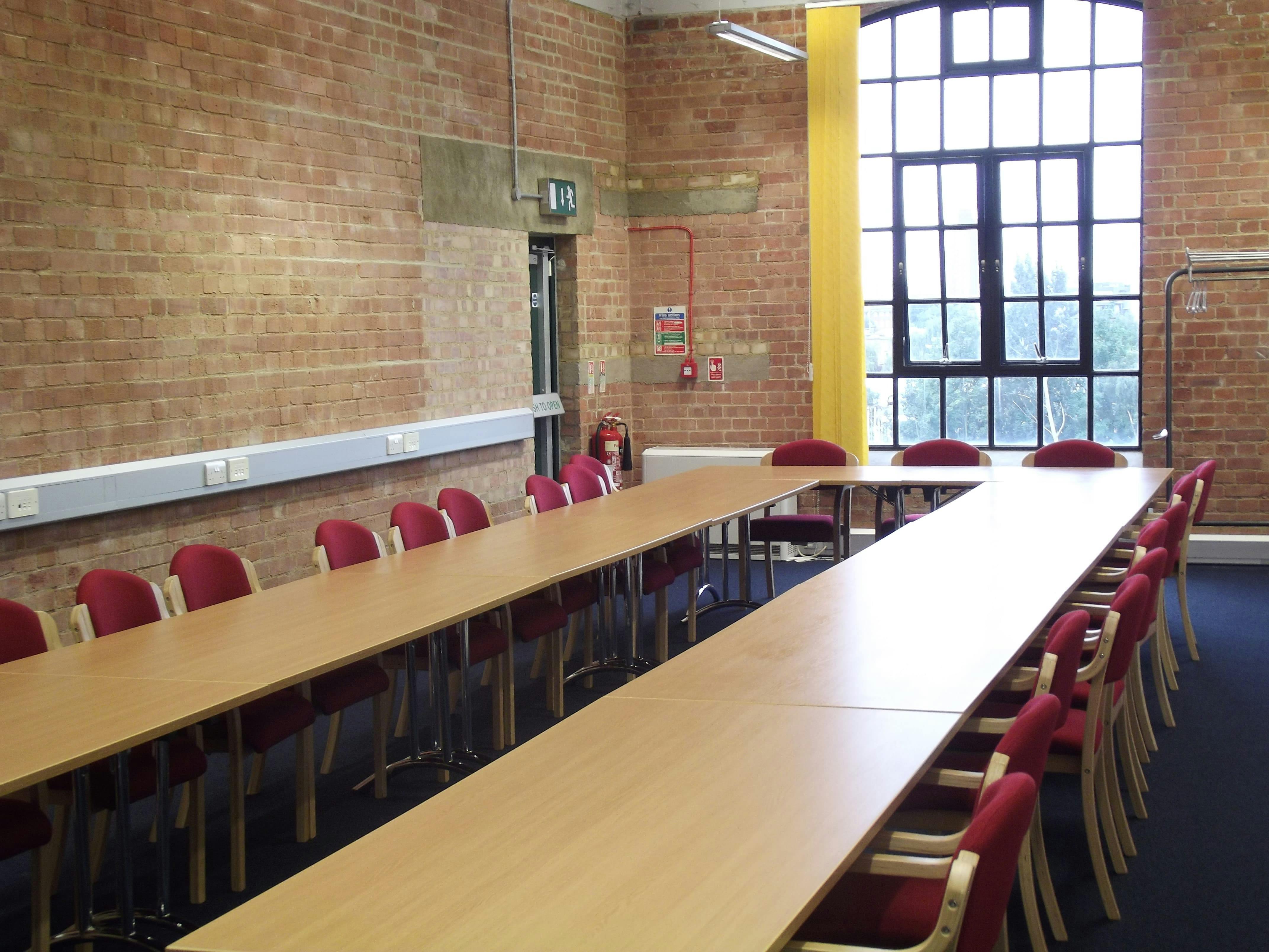 Versatile meeting room with long table, red chairs, ideal for workshops and team meetings.