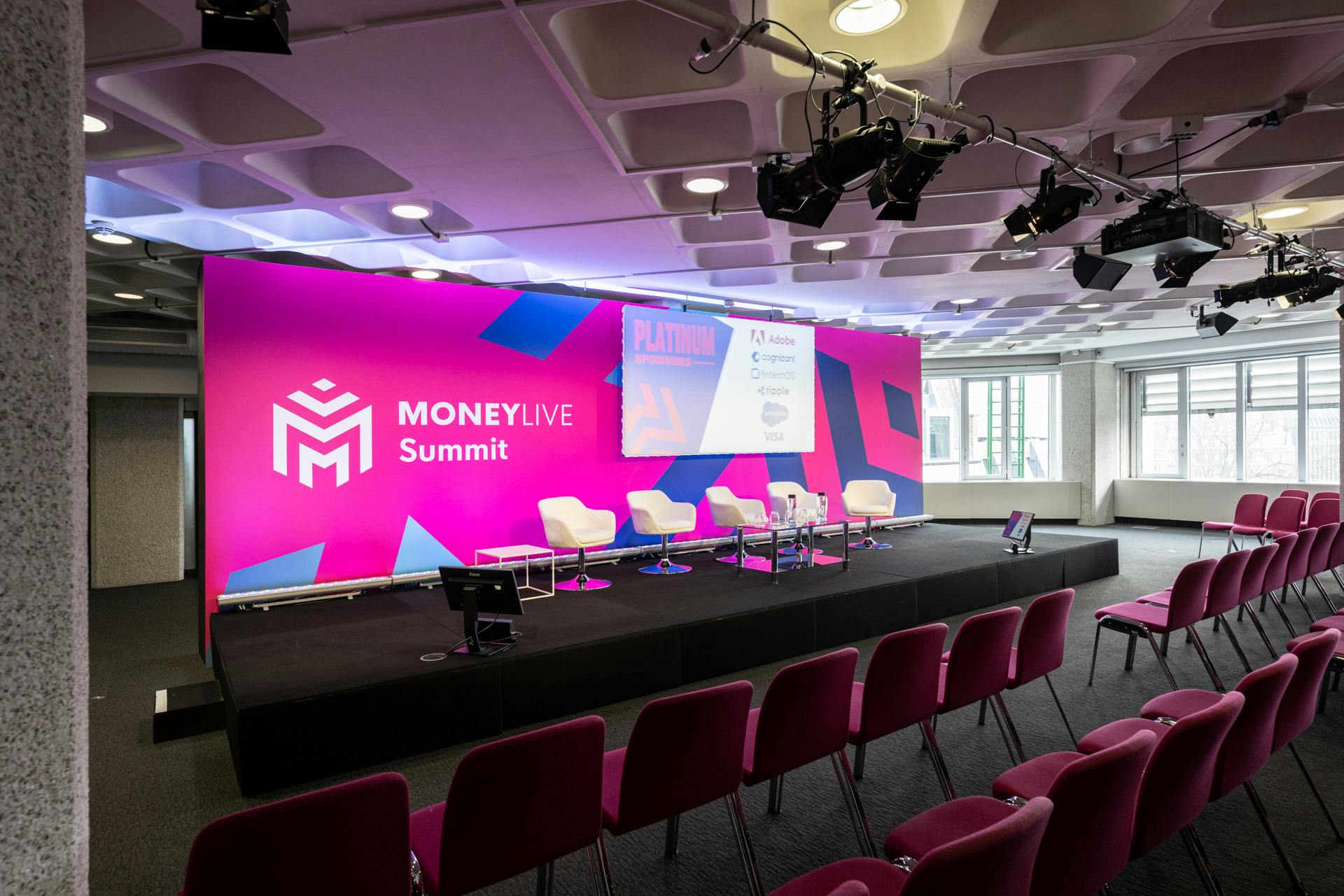 Event space at QEII Centre for MoneyLive Summit with vibrant pink backdrop.