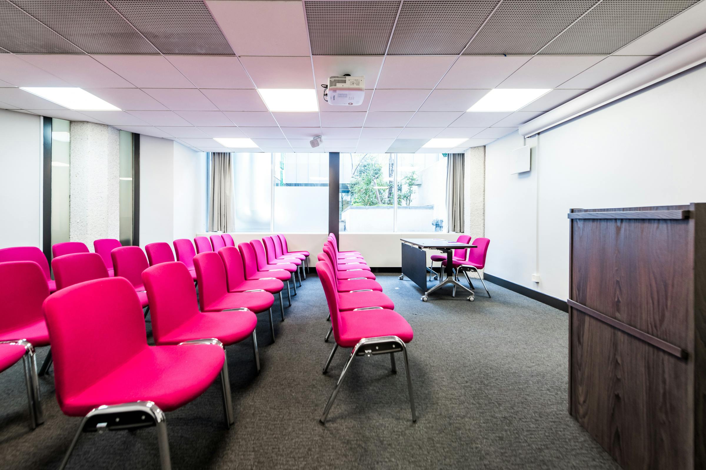 Modern meeting room with pink chairs, ideal for workshops and presentations.