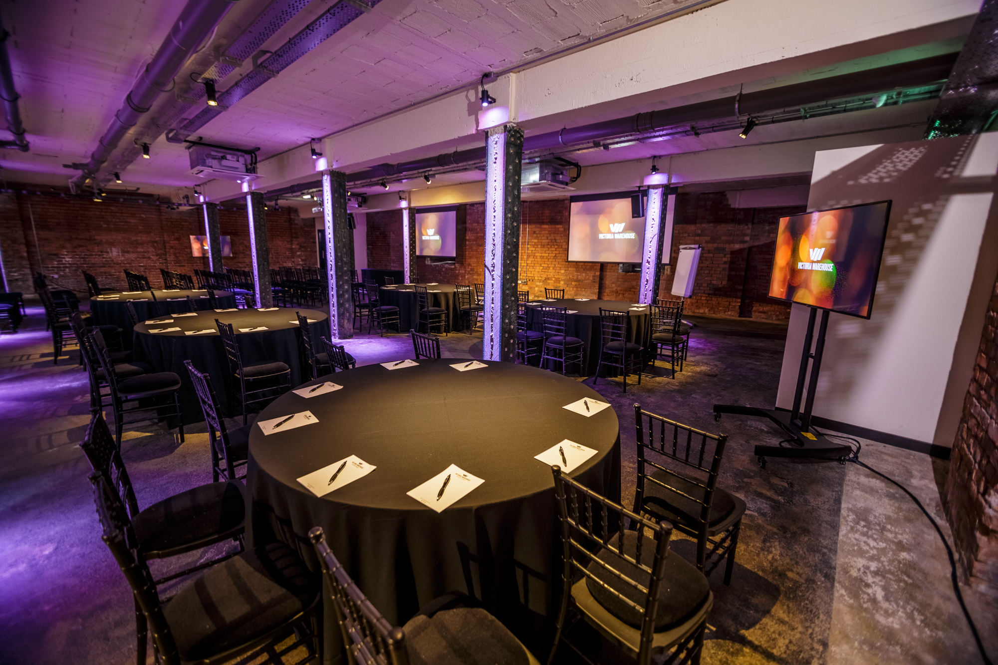 Versatile meeting space at Victoria Warehouse with round tables and ambient lighting.