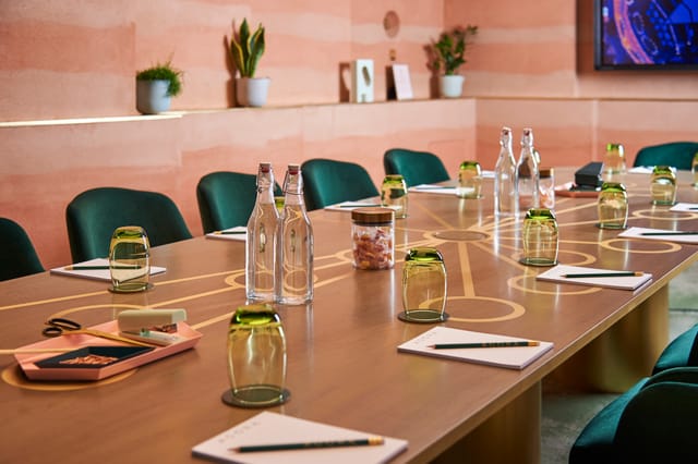 Modern meeting room at AGORA, Hilton London Bankside with wooden table and green chairs.