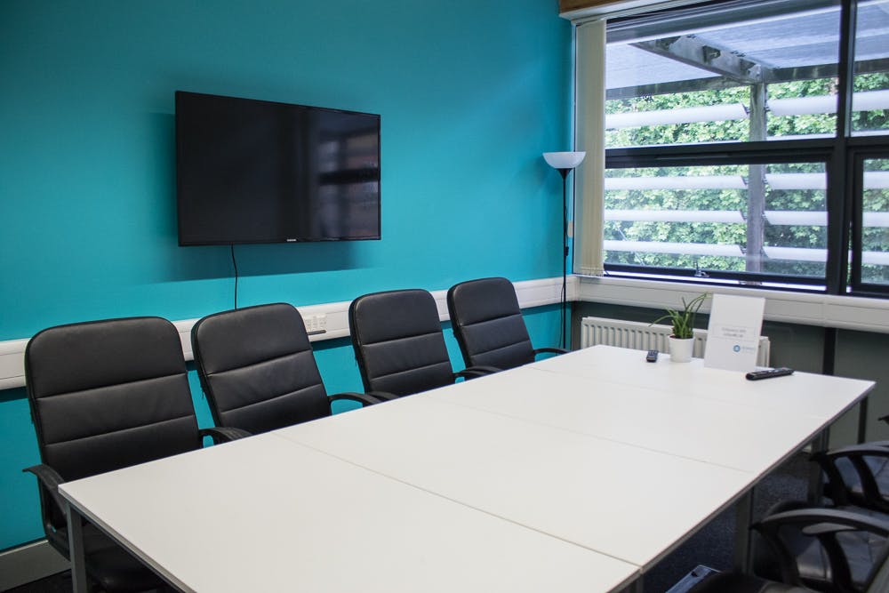 Modern meeting room with large white table, turquoise wall, ideal for collaboration.