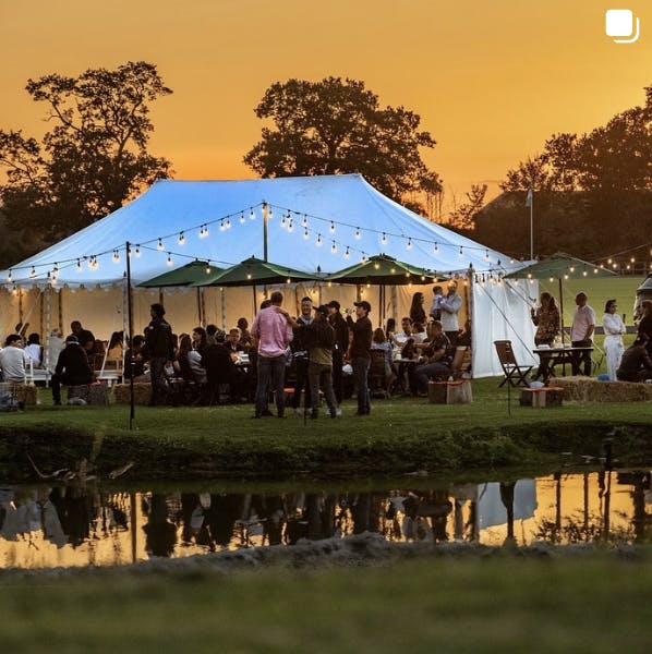 Outdoor wedding reception under a tent with string lights at Emsworth Polo Grounds.
