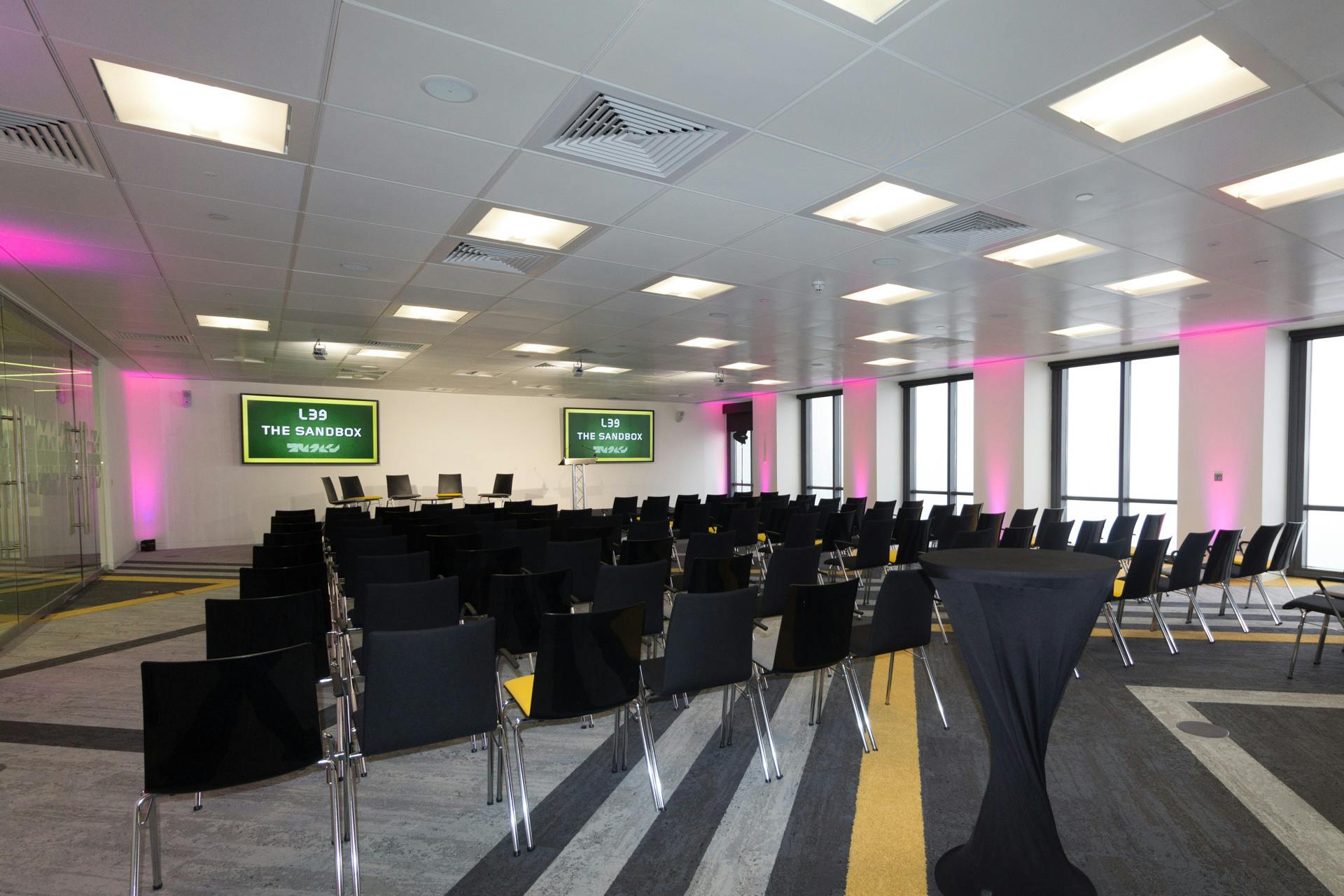 Modern event space with black chairs and pink lighting for presentations and networking.