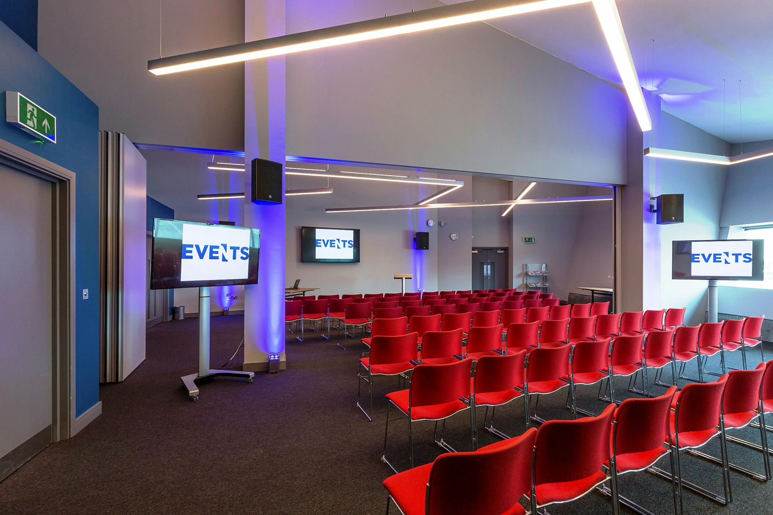 Modern event space with red chairs and dual screens at Imperial War Museum North.