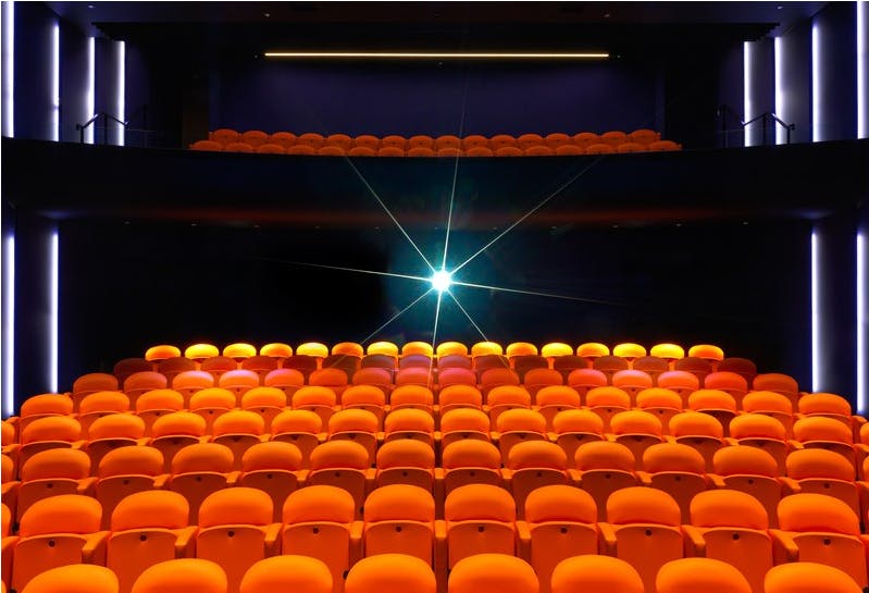 Modern auditorium with vibrant orange seating, ideal for presentations and performances.