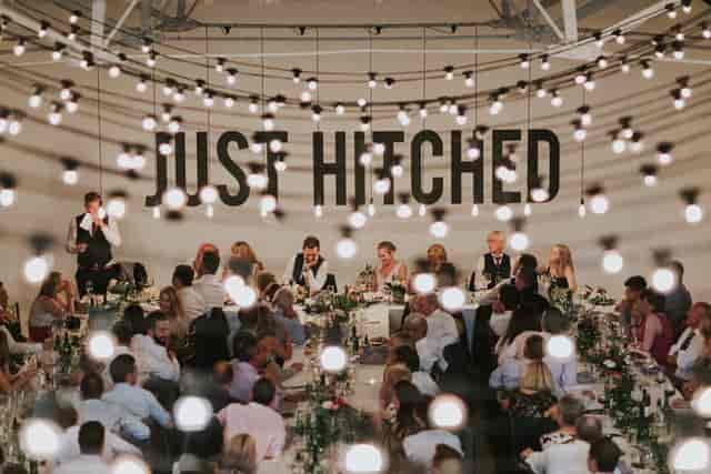 Wedding reception in Shoreditch Studios with "JUST HITCHED" backdrop and string lights.