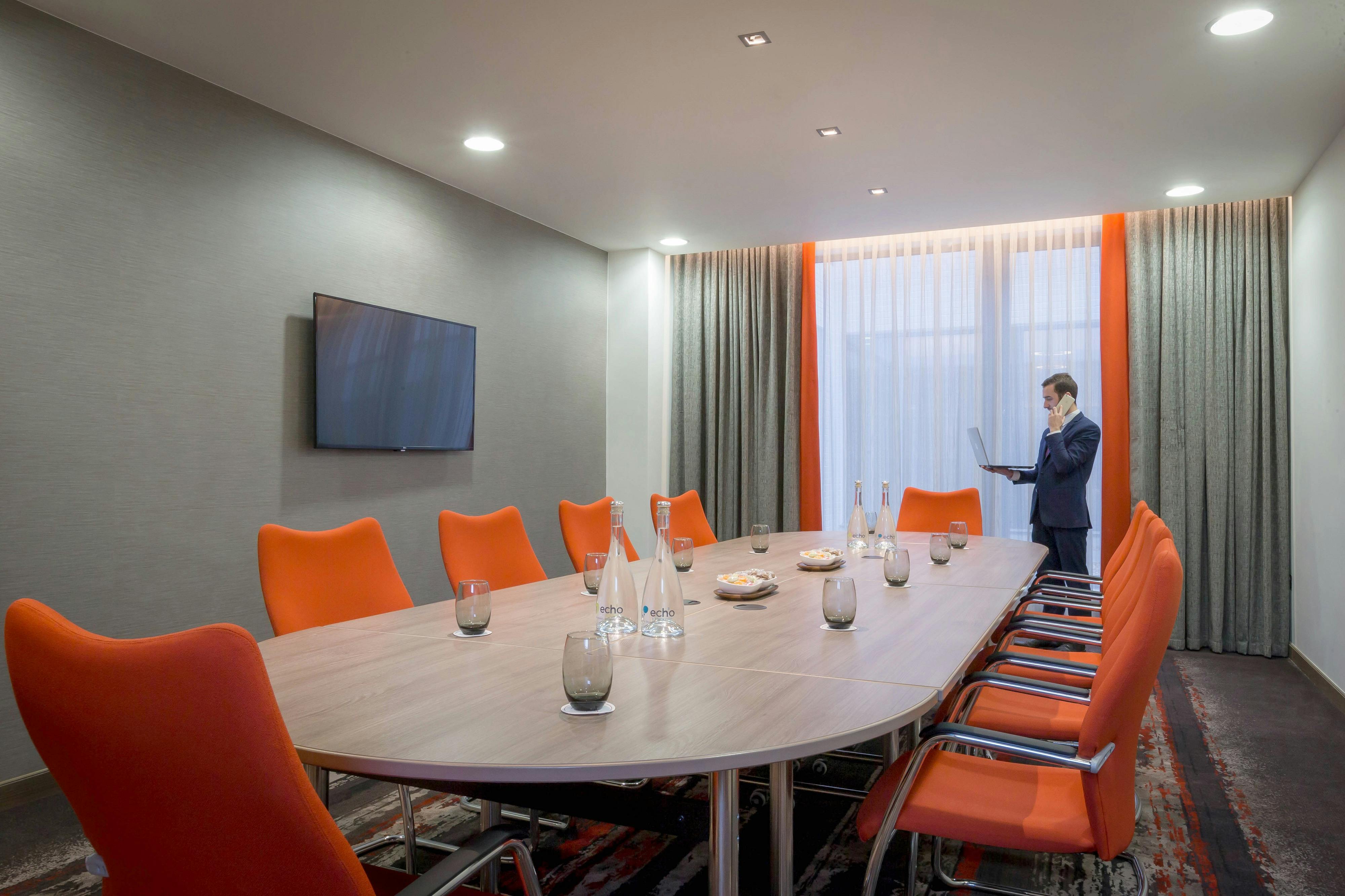 Modern meeting room in Bedford Suite, Clayton Hotel Chiswick, with oval table and orange chairs.