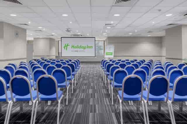 Meeting space with blue chairs and projection screen at Holiday Inn London Kensington.