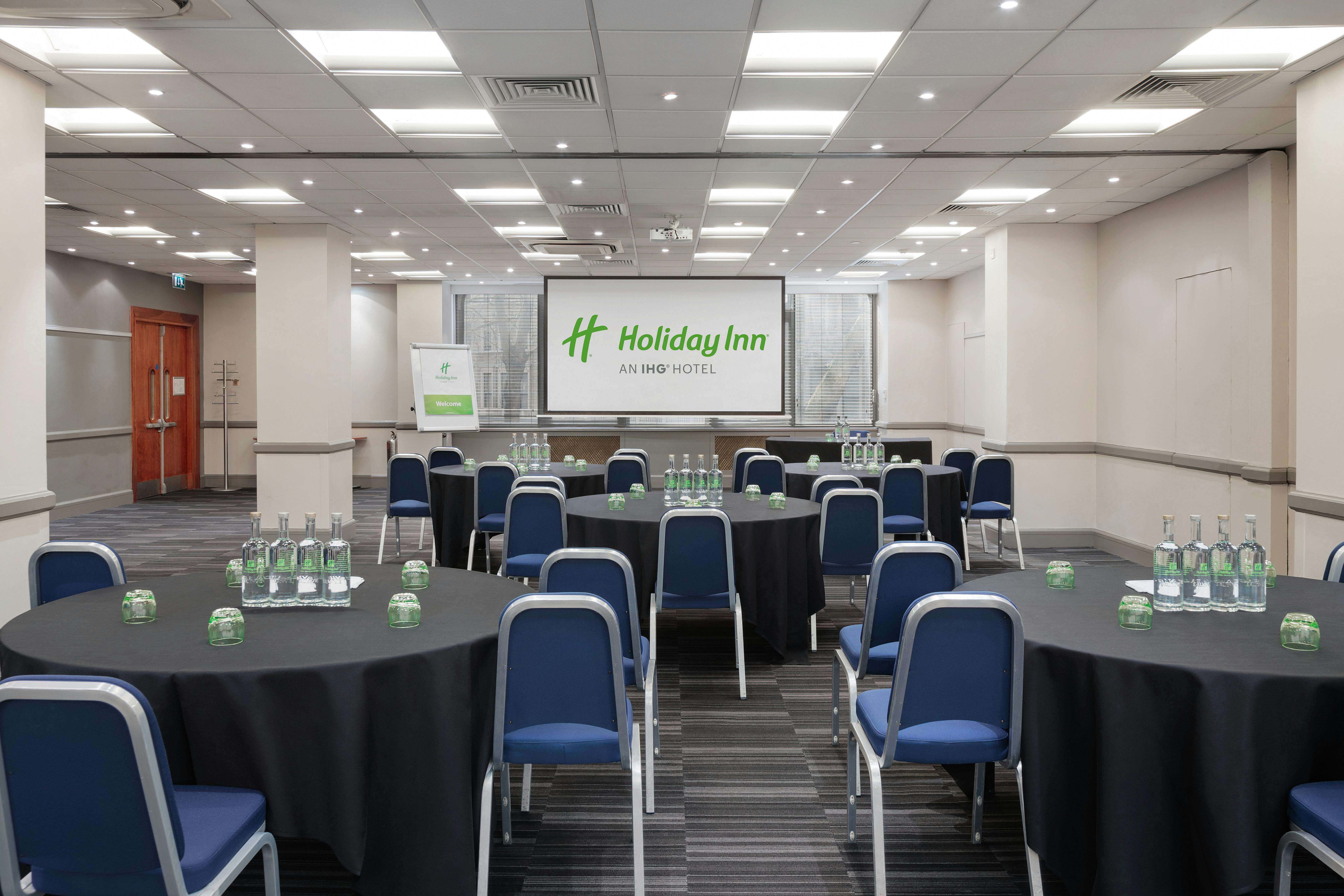 Meeting room at Holiday Inn Kensington, featuring round tables and modern lighting for conferences.