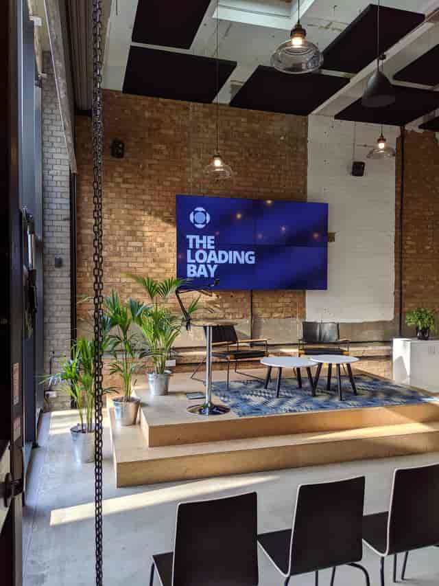 Modern event space "The Loading Bay" with large screen, ideal for corporate meetings and creative events.