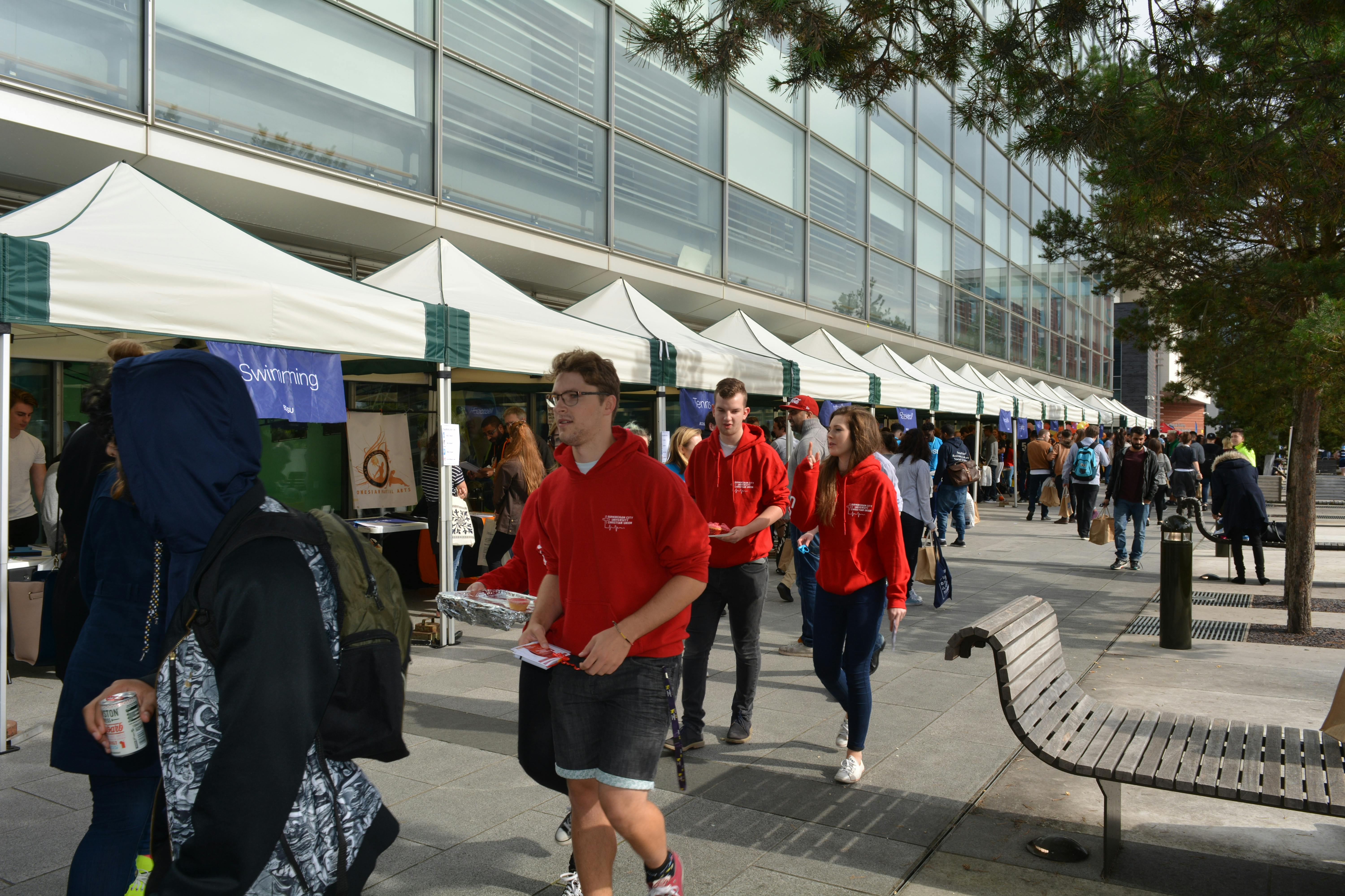 Outdoor event at Millennium Point with vibrant red-shirted staff and networking booths.