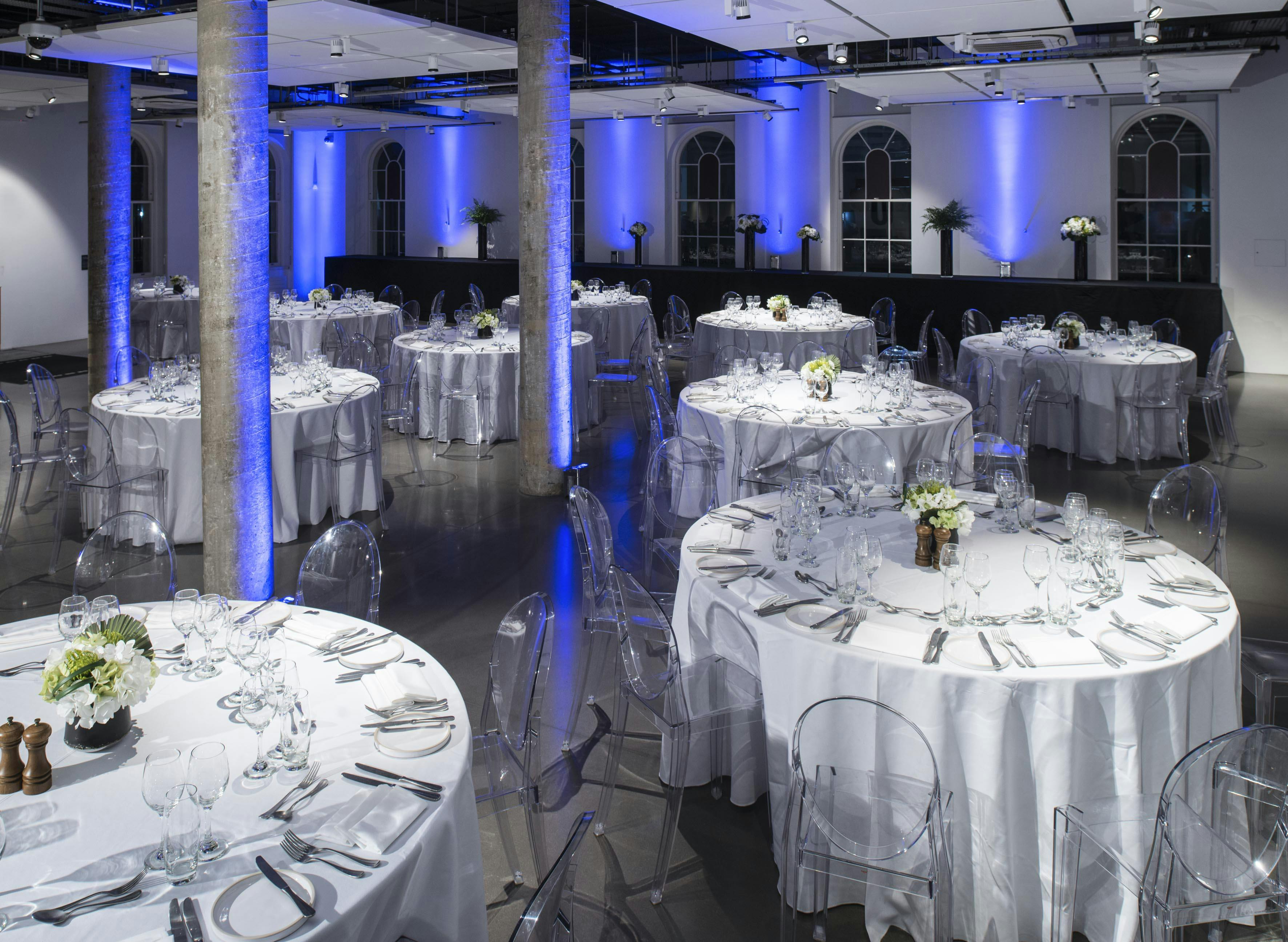 Elegant event space in Science Gallery London, set for formal dinner with blue lighting.