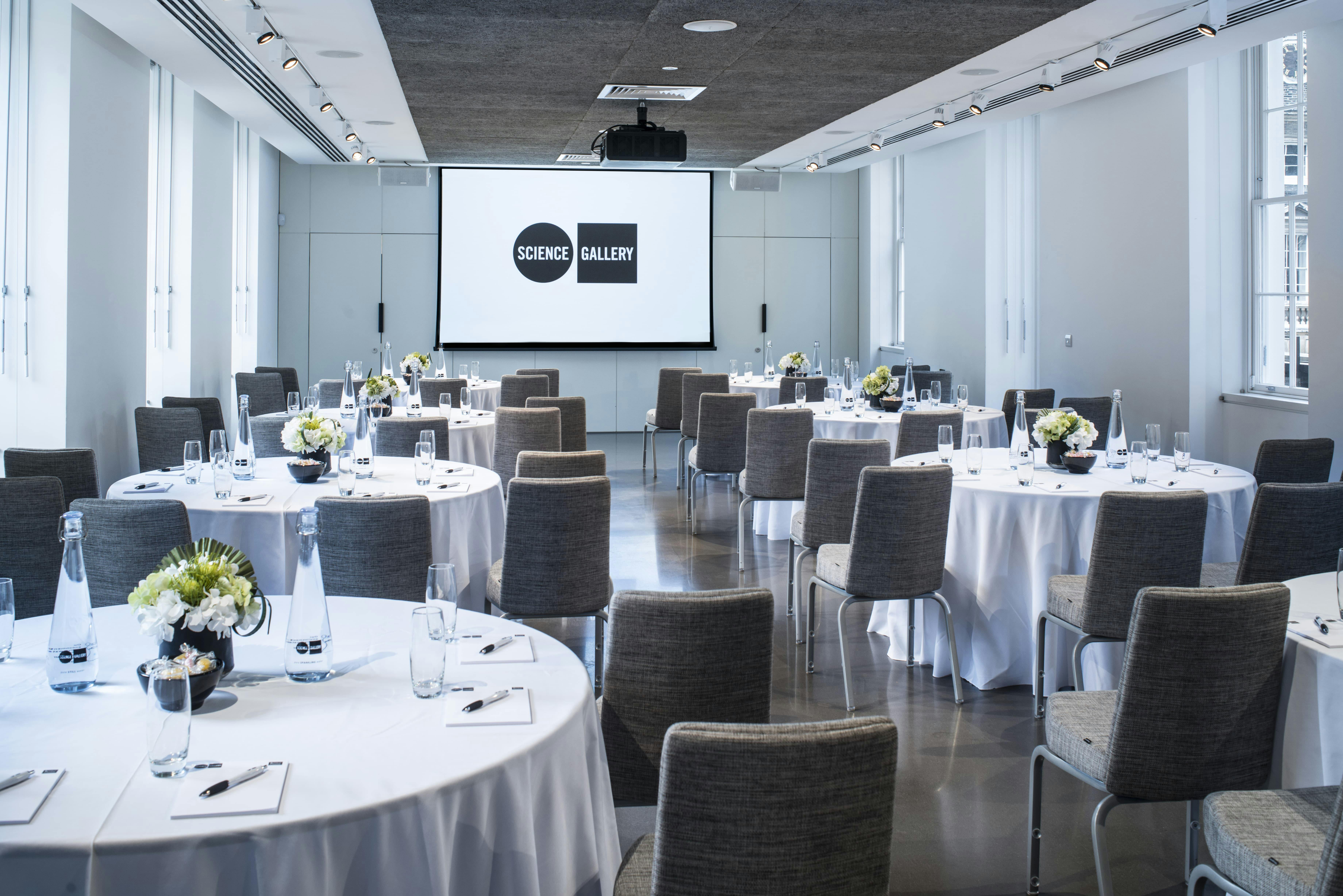 Meeting space with round tables and large screen at Science Gallery London for professional events.