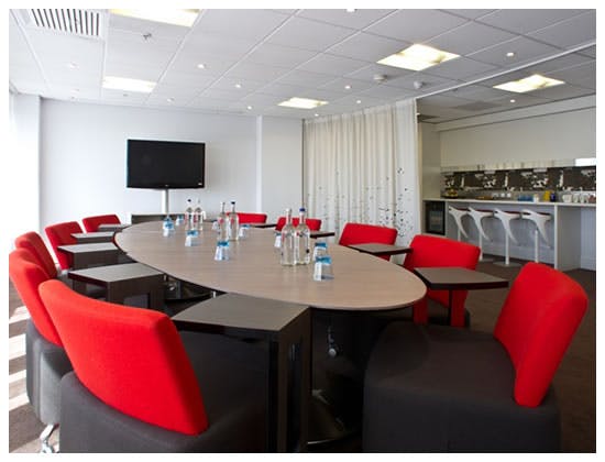 Modern meeting room with oval table and red chairs, perfect for workshops and strategic meetings.