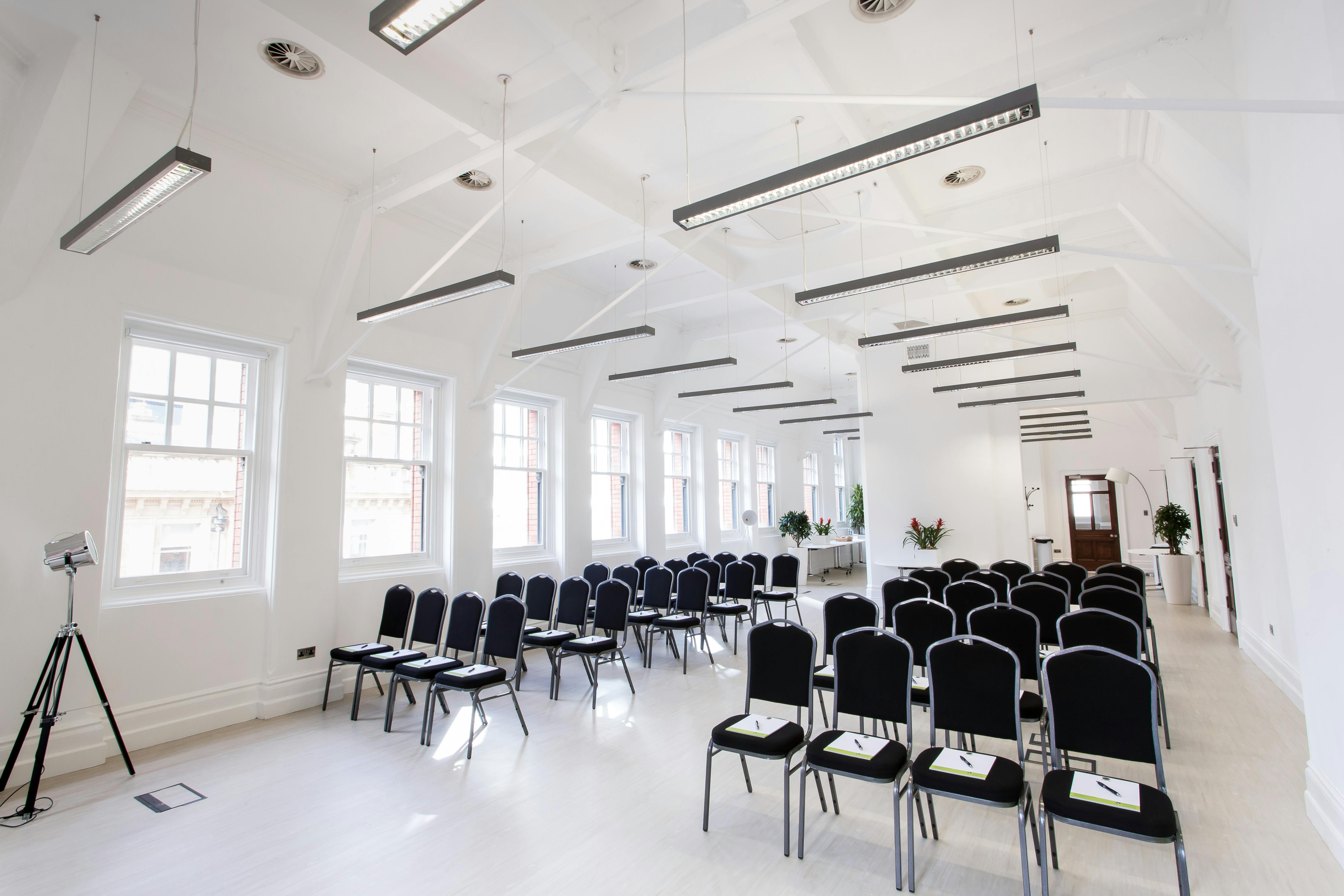 Modern White Room event space with black chairs, ideal for meetings and presentations.