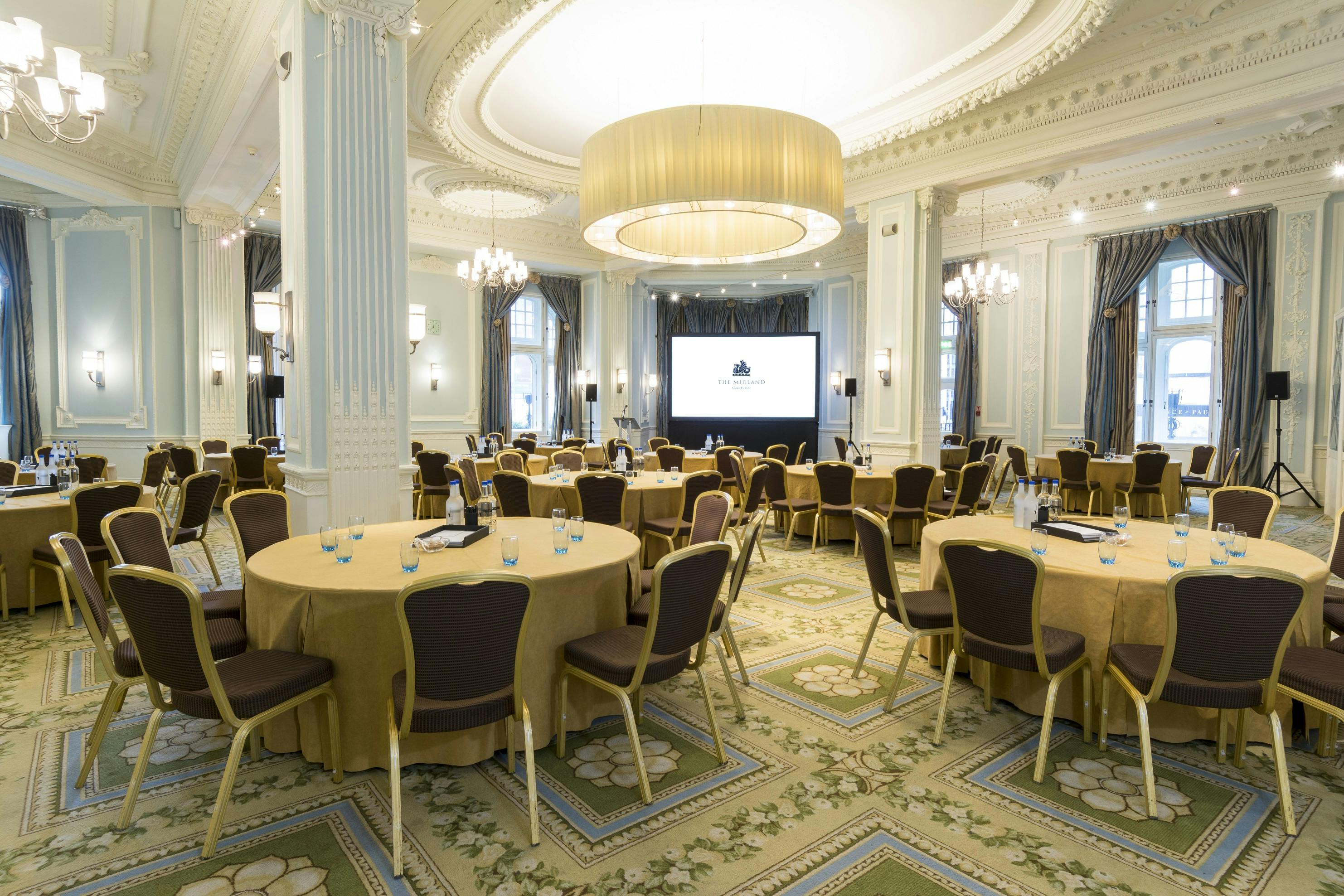 Elegant conference space at The Trafford, featuring gold-draped tables and presentation screen.