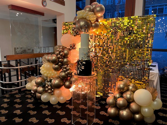 Elegant cake display with gold and white balloons at The Charter Gallery event. - Banner