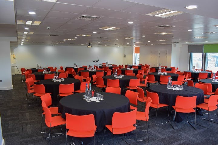 Event space in thestudio Glasgow with round tables, orange chairs for corporate gatherings.