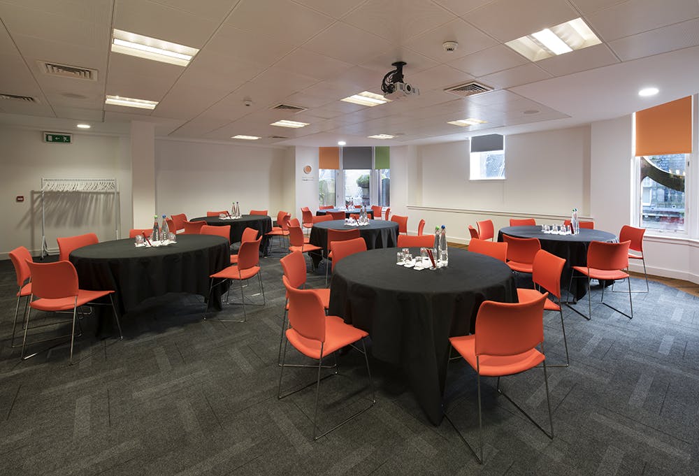 Versatile meeting space in Glasgow with round tables and bright orange chairs for networking events.