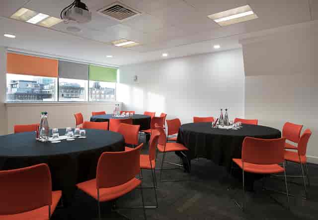 Meeting room at Shout in Glasgow, featuring round tables and vibrant orange chairs for workshops.