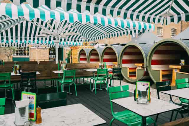 Outdoor terrace dining at Pizza Pilgrims with colorful seating and striped canopies.