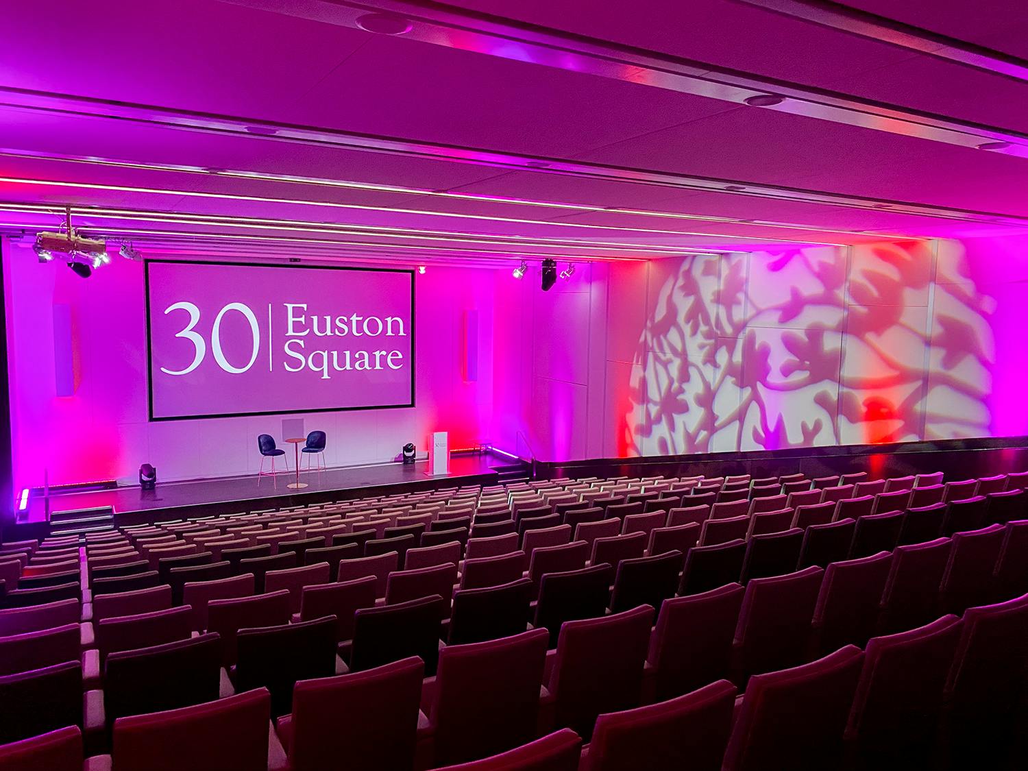 Modern auditorium with tiered seating and pink lighting for conferences at 30 Euston Square.