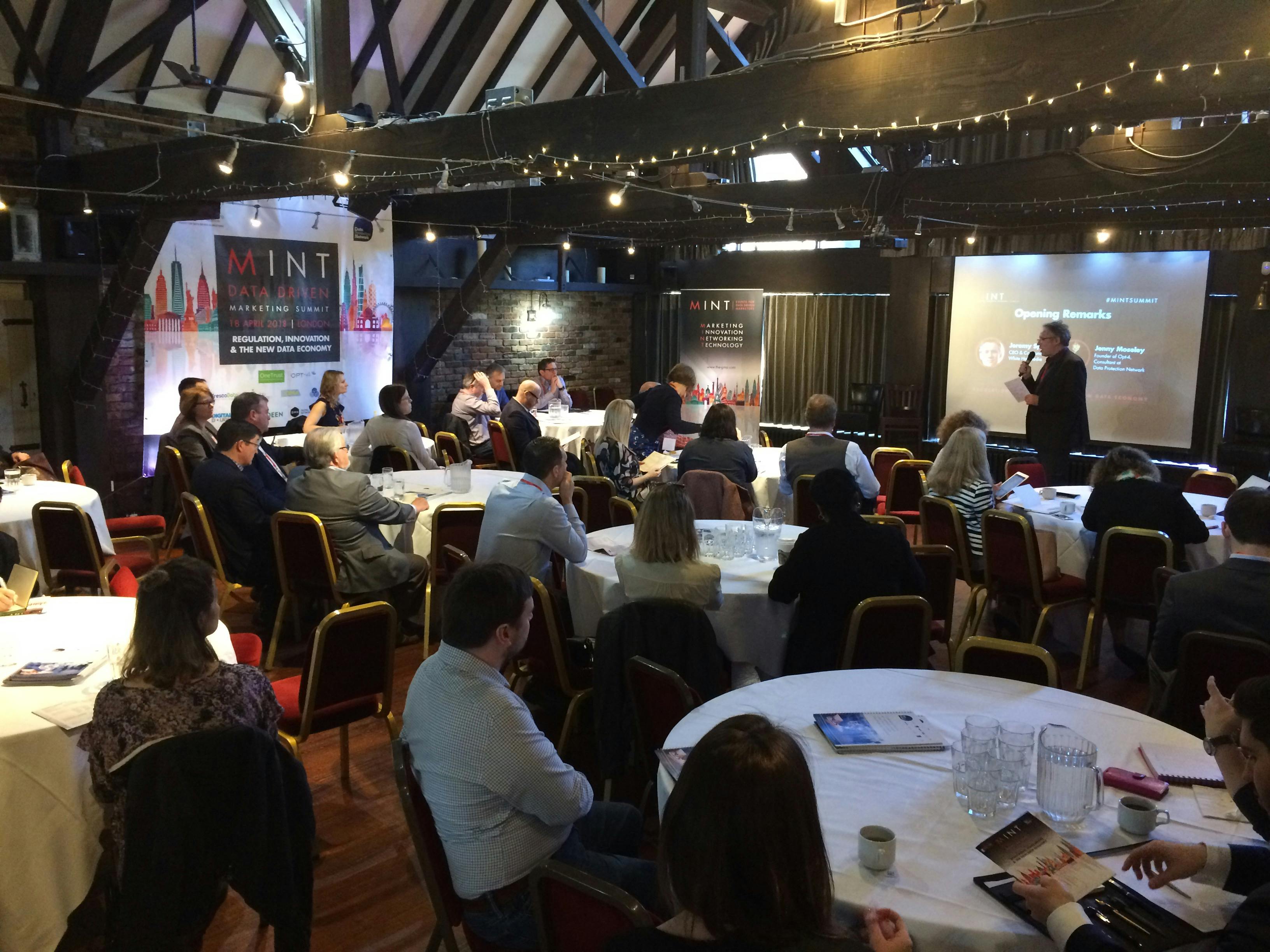 Conference setting in Dickens Inn with speaker engaging attentive audience at round tables.