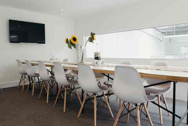 Modern boardroom with wooden table, white chairs, ideal for meetings and brainstorming.
