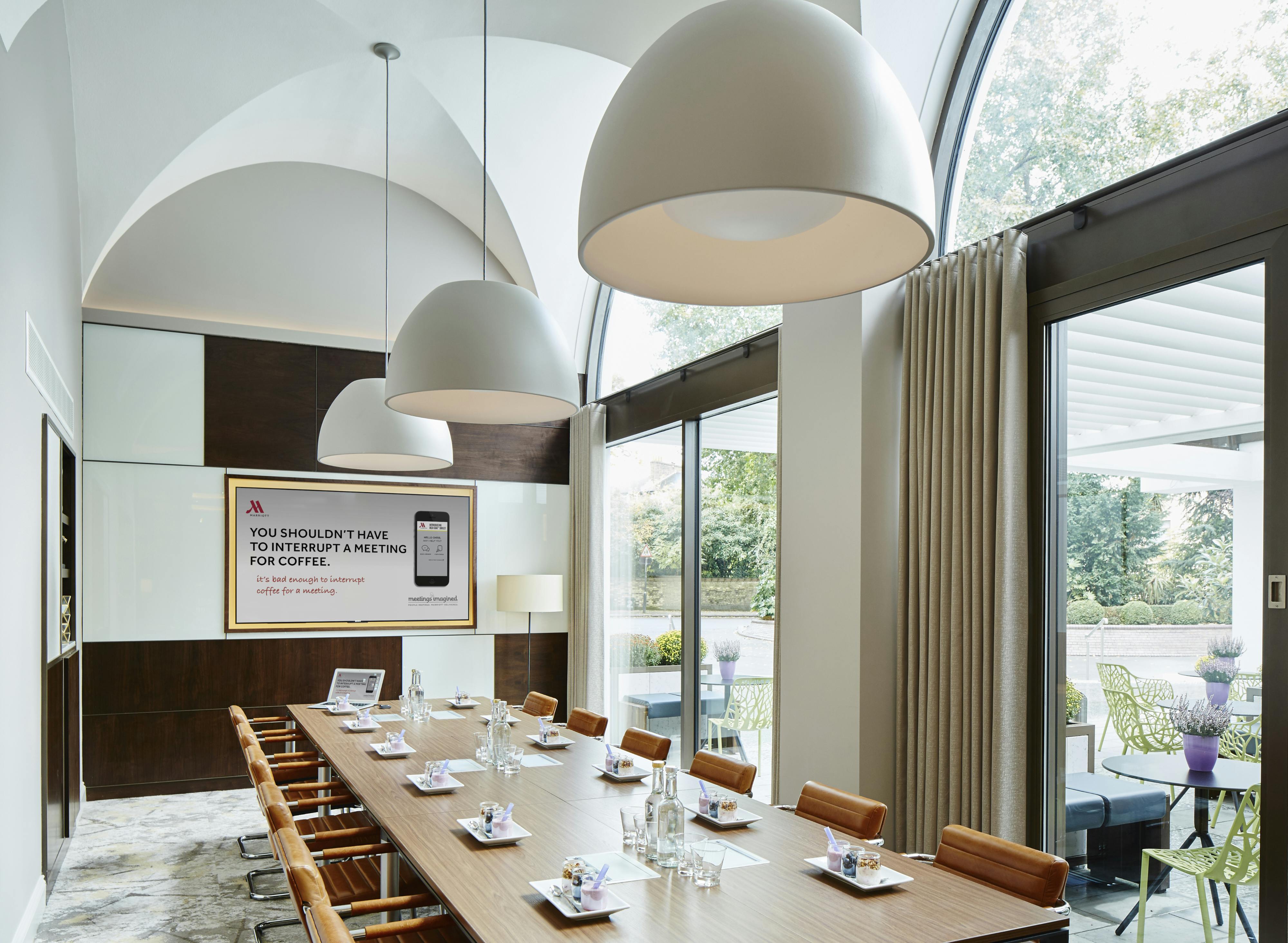 Modern meeting room at London Marriott, featuring natural light and digital screen for events.