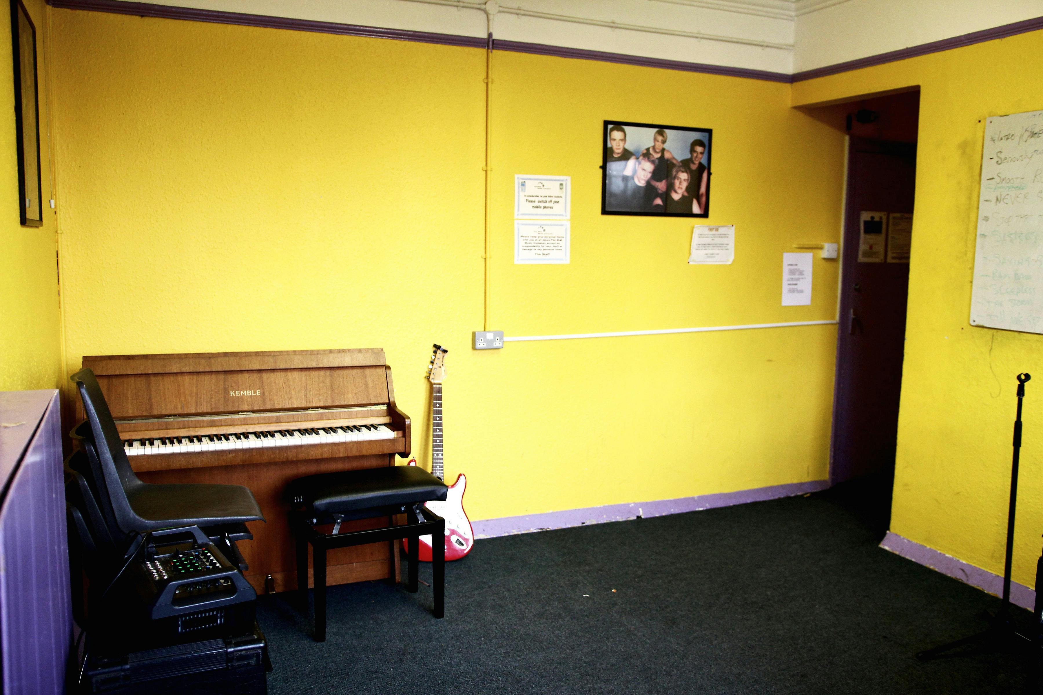 Vibrant rehearsal space with yellow wall, piano, and guitar for creative workshops.