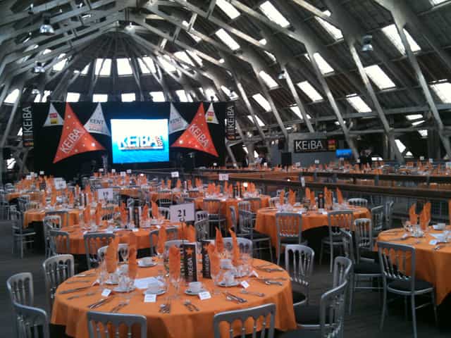 Banquet setup in Slip Mezzanine, Historic Dockyard with orange tablecloths and high ceiling.