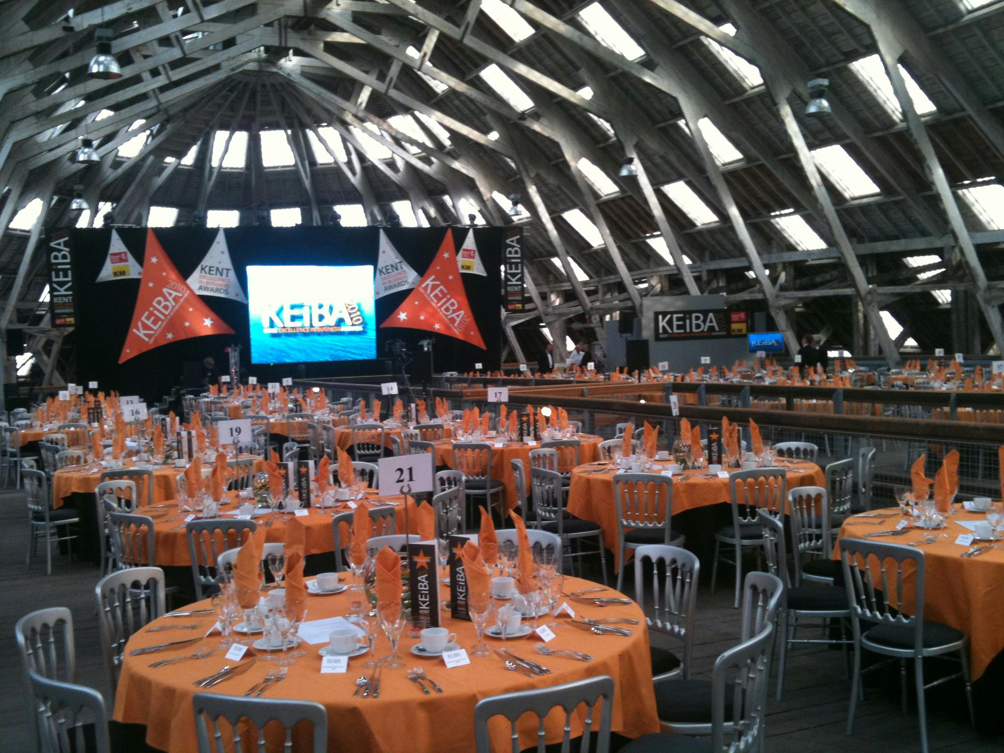 Banquet setup in Slip Mezzanine, Historic Dockyard with orange tablecloths and high ceiling.