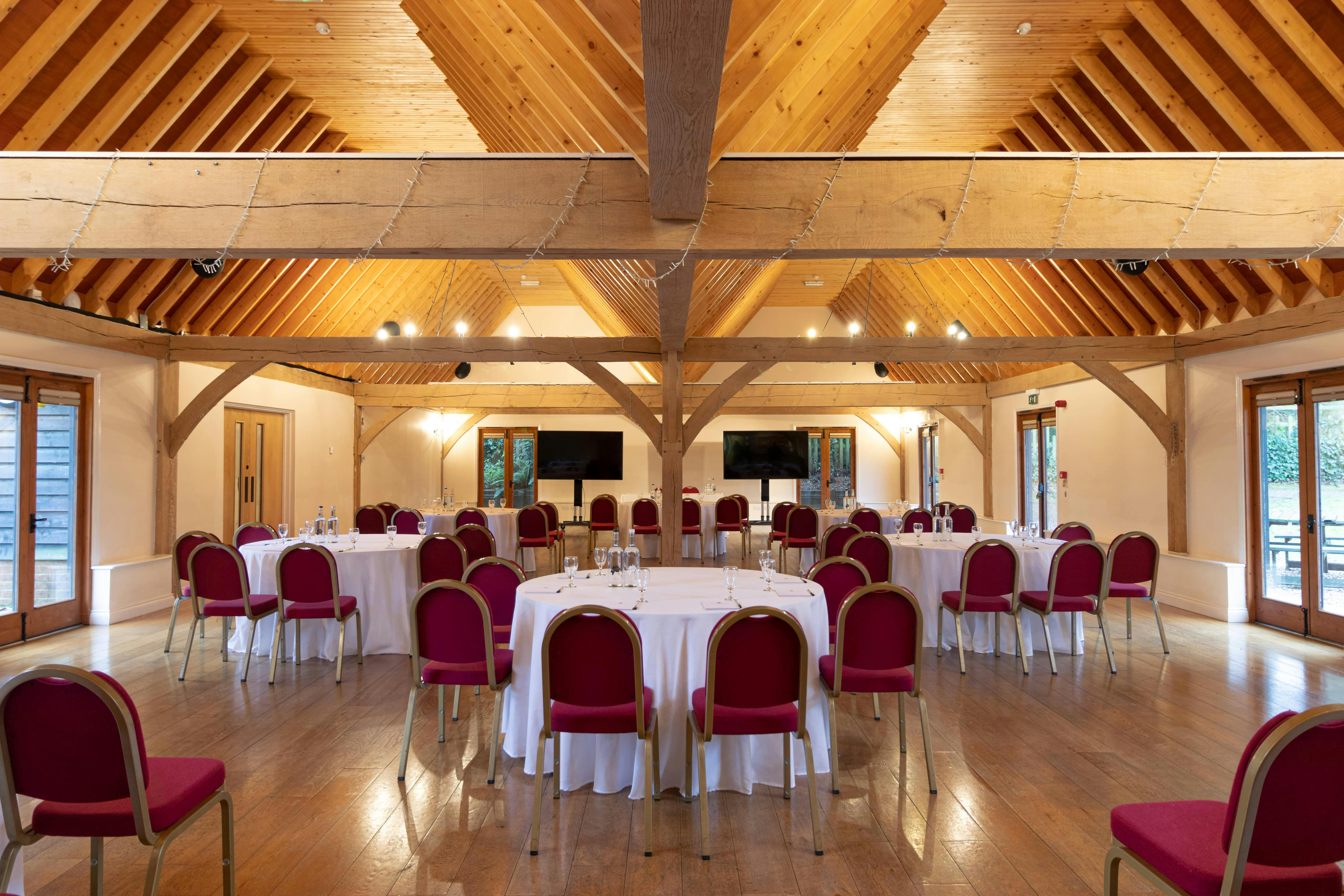 Cobbold Barn event space with round tables and red chairs, perfect for meetings and presentations.