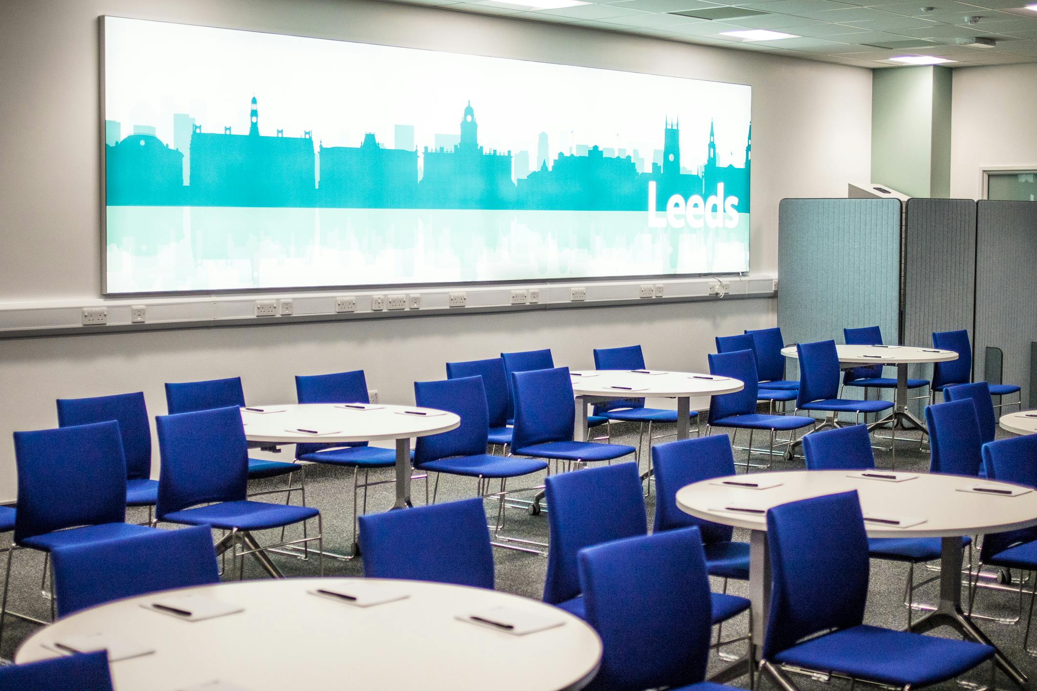 Modern meeting space in Leeds with round tables and blue chairs for corporate events.