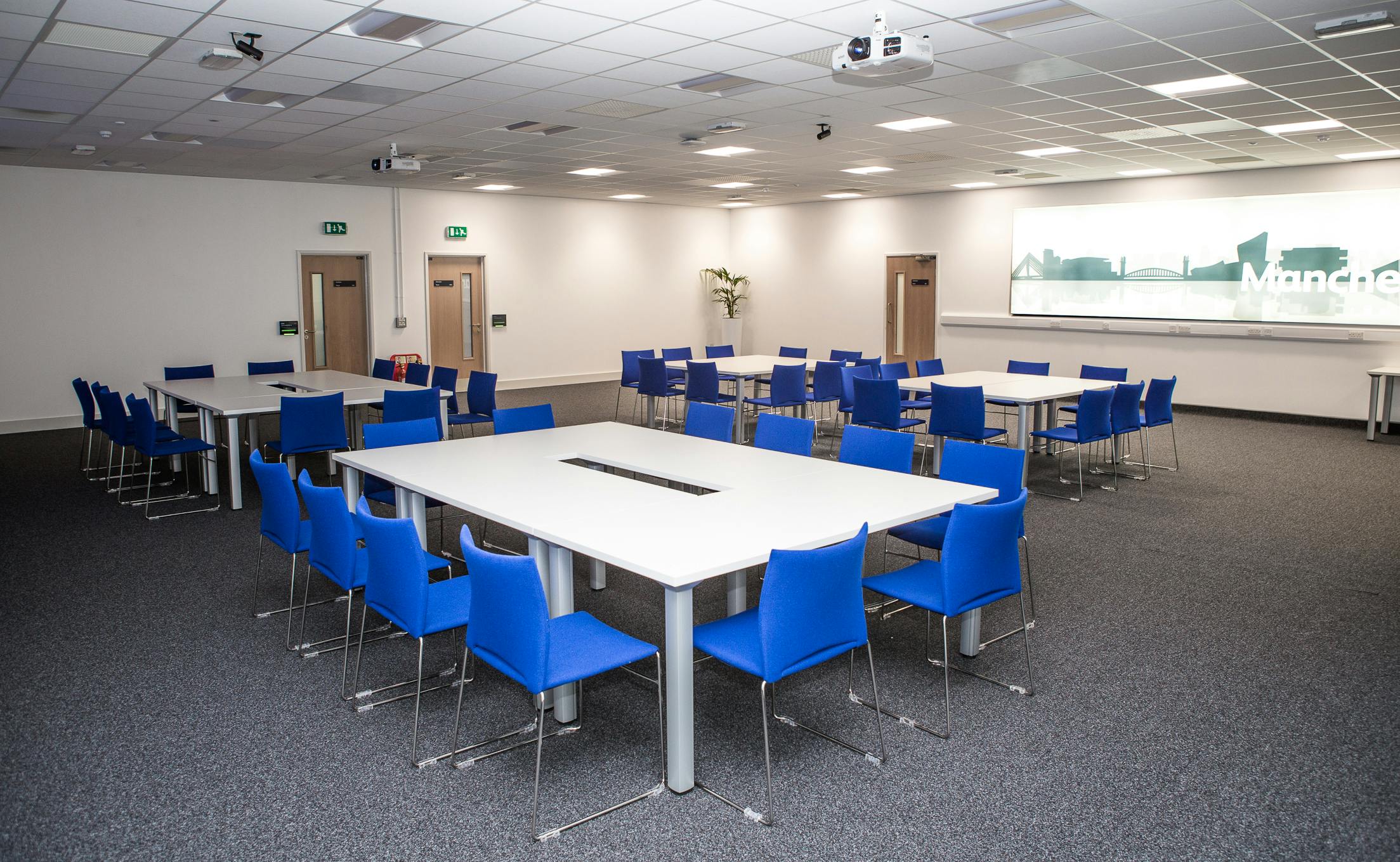 Versatile meeting space with modular tables and blue chairs for workshops and presentations.