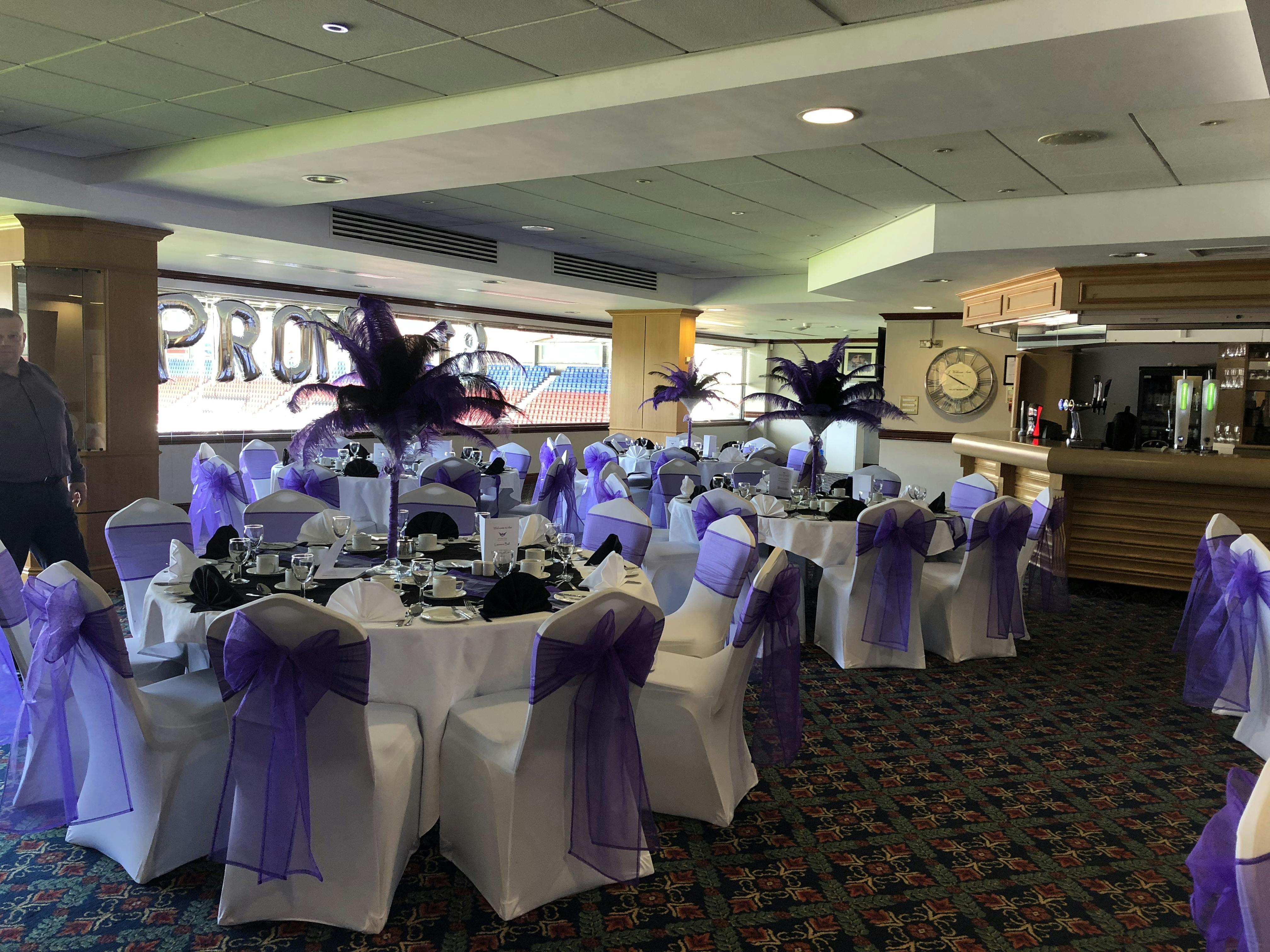 Elegant event space at Phoenix Lounge, DW Stadium with white linens and purple sashes.