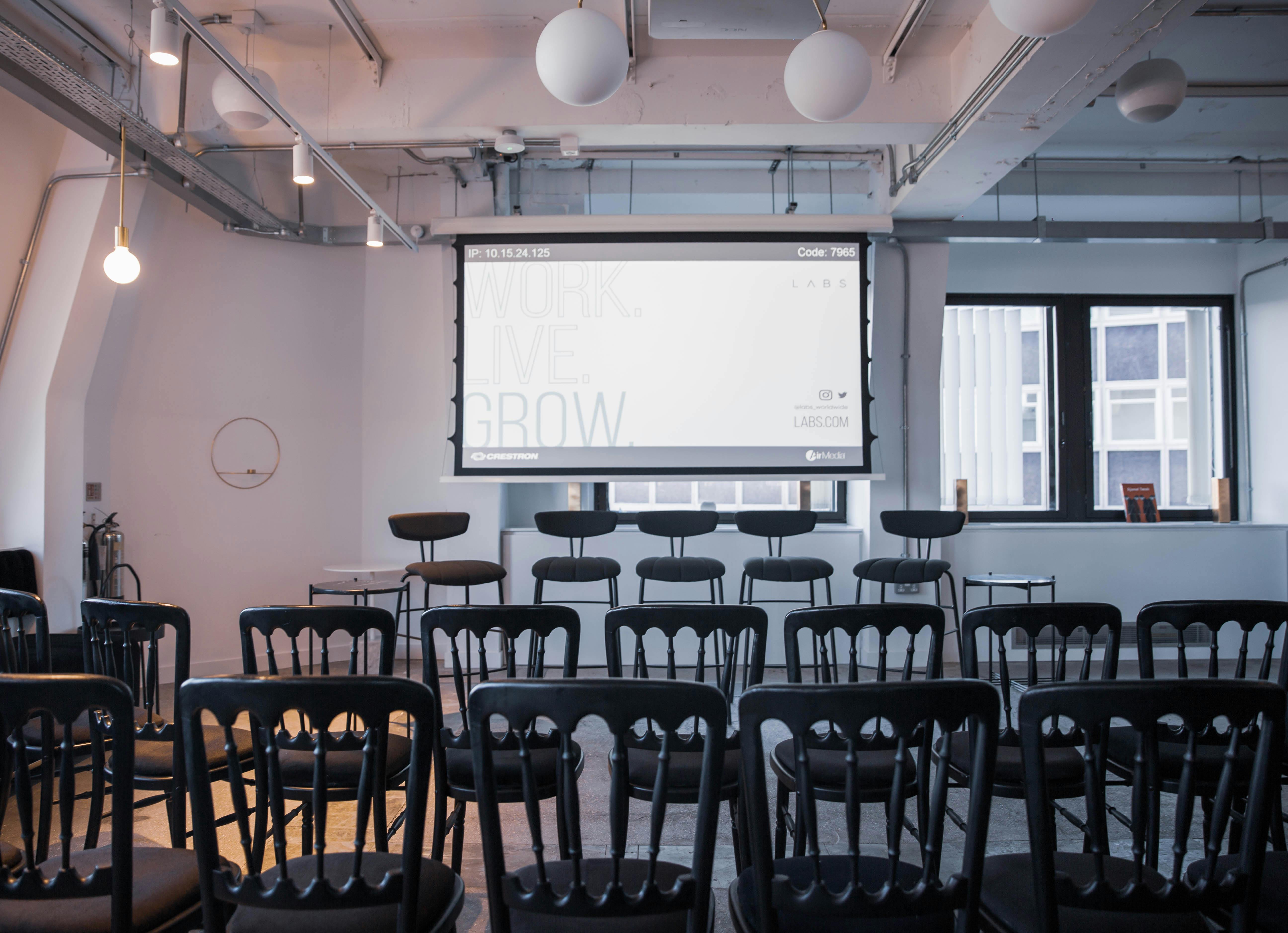 Modern event space with black chairs and large screen for presentations at LABS House Holborn.