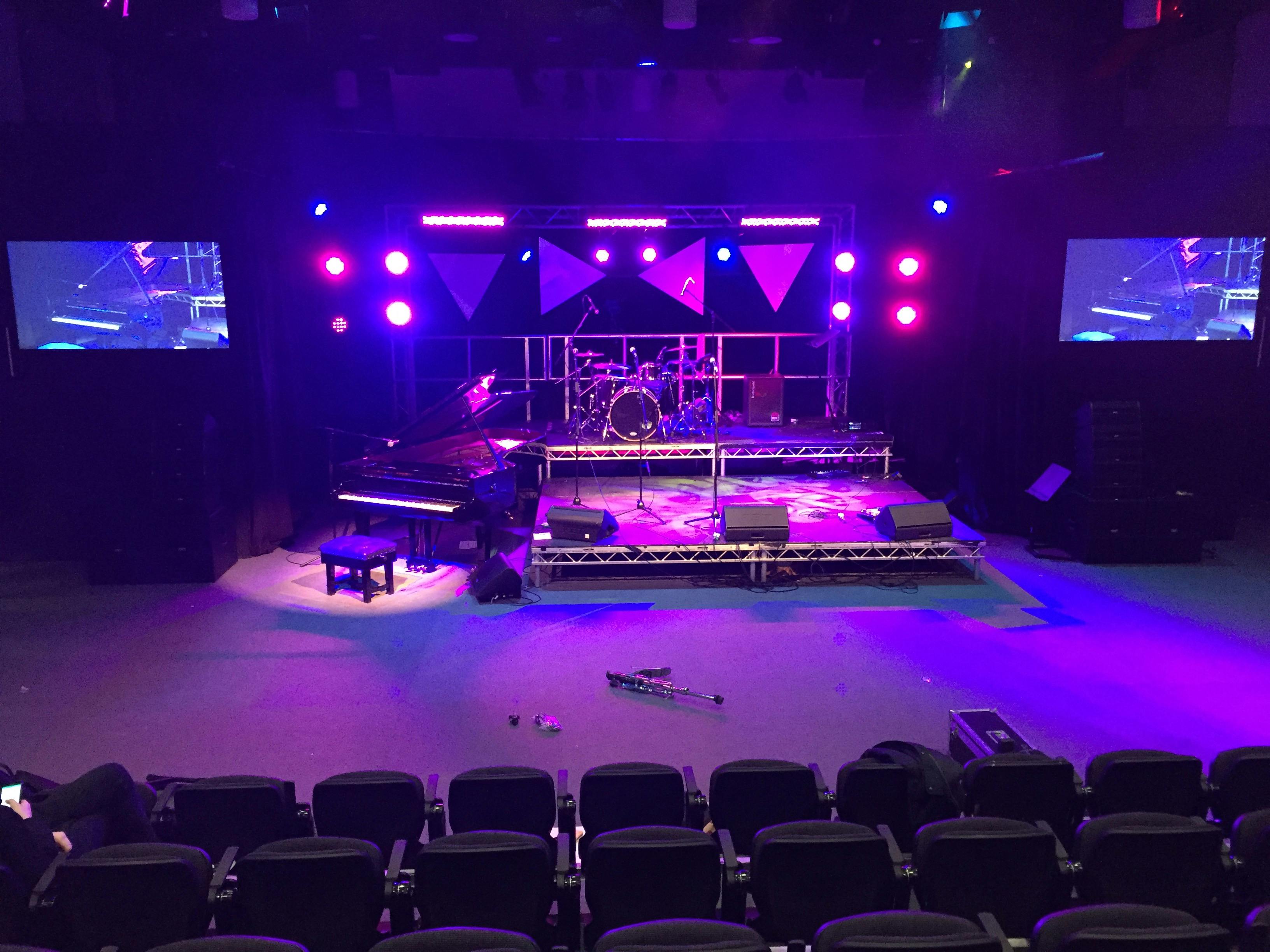 Weston Hall stage setup with grand piano and drum kit for live concert event.