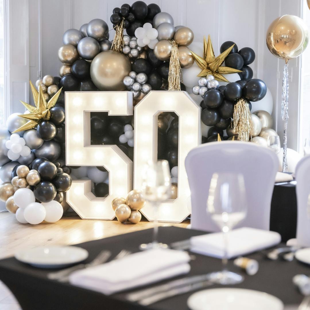 Elegant 50th birthday setup with illuminated "50" and black, gold, white balloons.