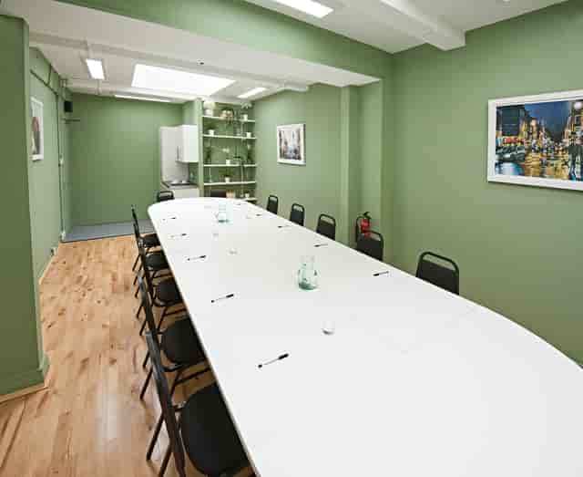 Modern meeting room at The Whitehall Studio, featuring a long white table and green walls.