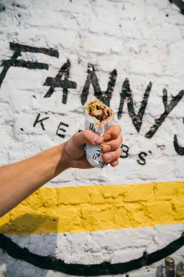 Hand holding a kebab sandwich at Fanny's Kebabs, perfect for casual dining events.