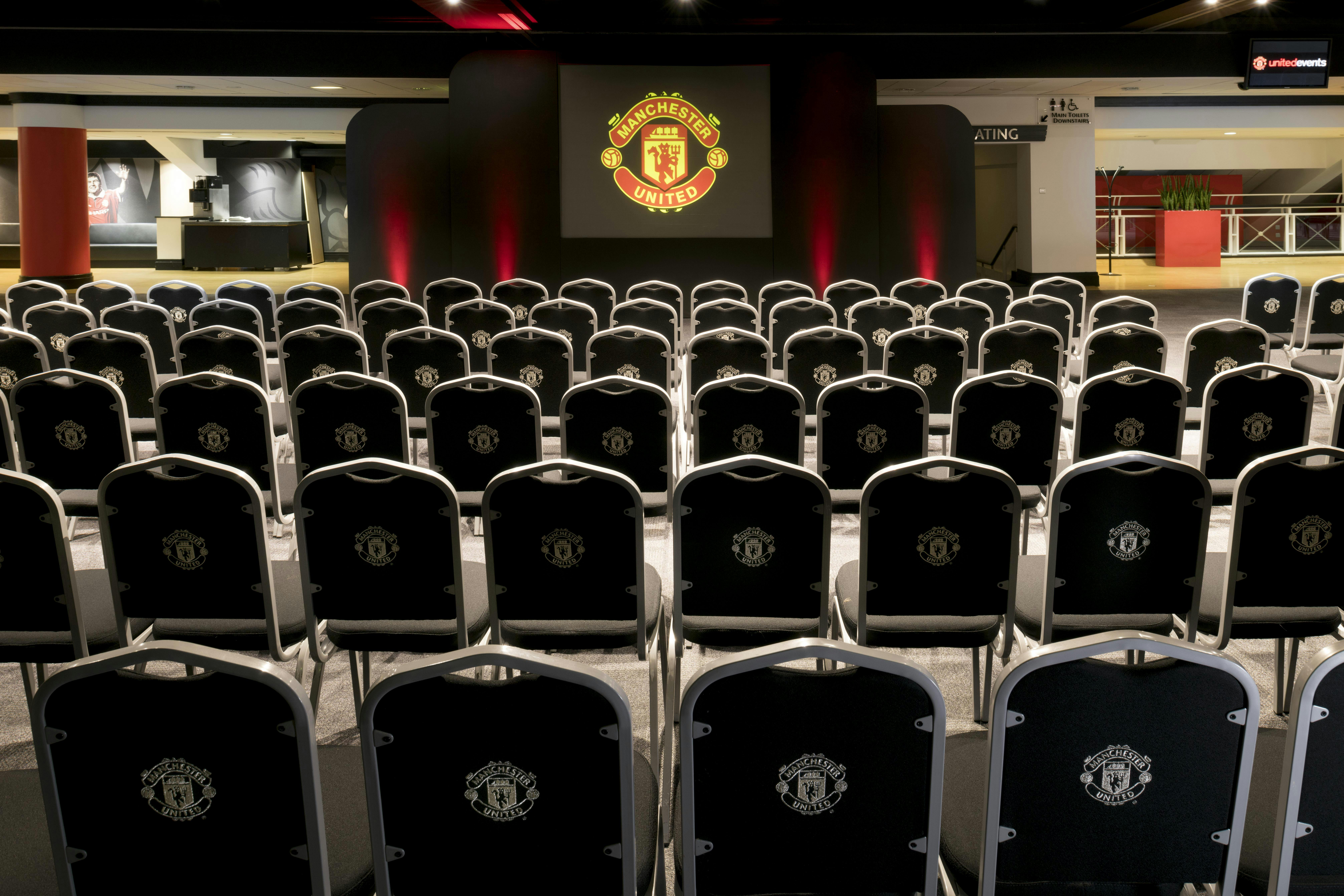 Conference event space at Old Trafford with branded chairs for corporate presentations.