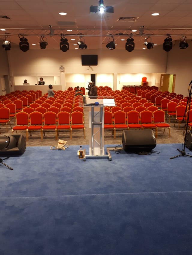Business conference room with podium and red chairs at Elim Pentecostal Church, Harlesden.