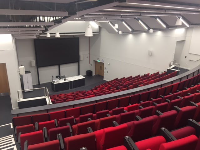 Modern auditorium with tiered red seating for conferences at ARU Venue Hire, Cambridge.