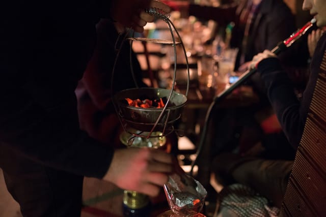 Cozy Maddox Club Mayfair garden with server preparing hookah for social events.