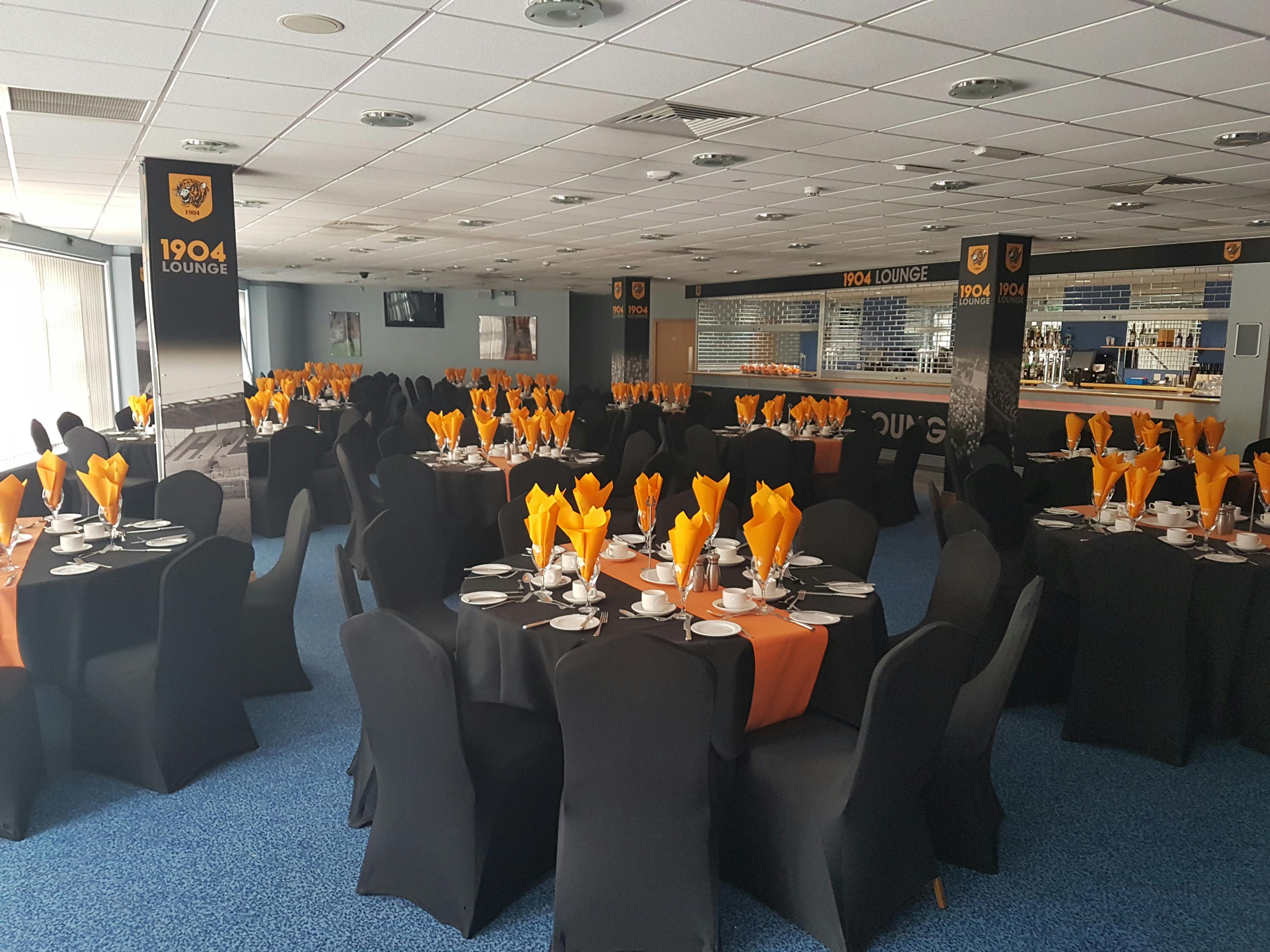 Elegant event space at MKM Stadium with black tables and orange napkins for corporate gatherings.