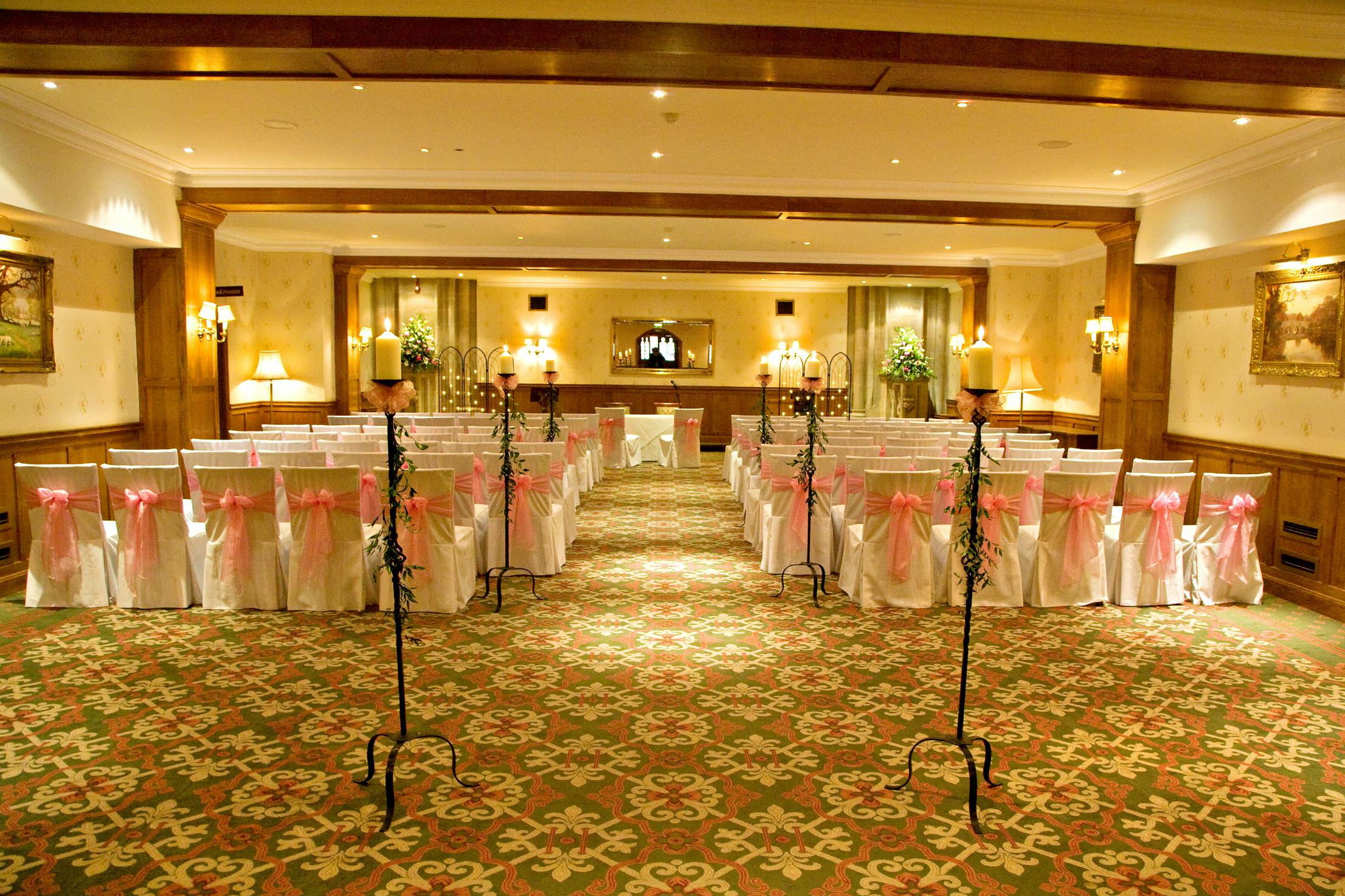 Harry Clarke in elegant wedding venue with pink-sashed chairs at Ashdown Park Hotel.