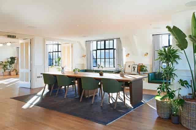 Bright meeting space with wooden table and green chairs in Mortimer House.